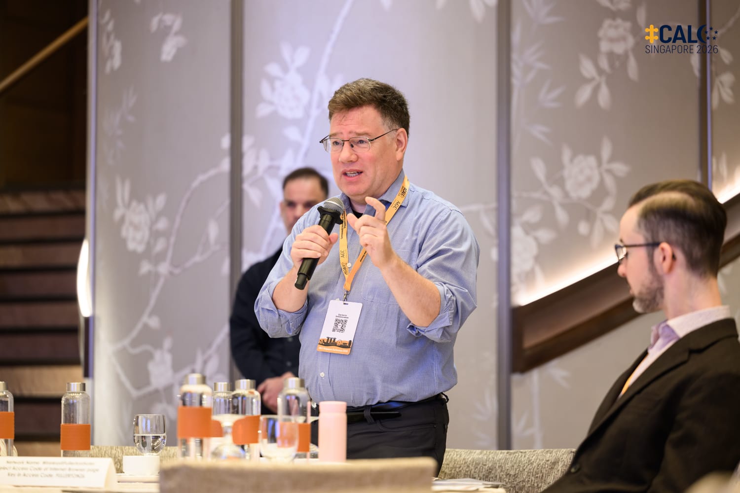 A delegate stands and speaks into a handheld microphone at the Conference in the ballroom at The Fullerton Hotel Singapore.
